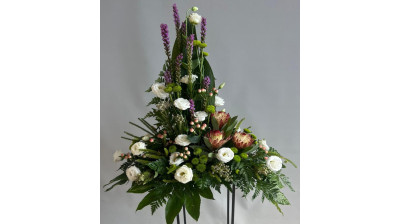 Centro de flores compuesto por helecho cuero, liatrix, aralia, aspidistra, lisianthus, protea, margarita, hypericum, leucadendro